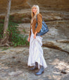 A blonde woman in a white dress standing in front of a rock wearing lace-up design Bed Stu Judgement boots.