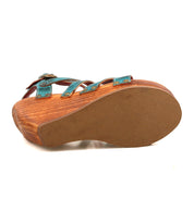 Bed Stu Juliana II is a wooden platform sandal featuring a tan rubber sole and teal leather strappy upper, shown here from the bottom.