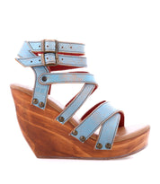 The Juliana II by Bed Stu is a light blue wedge sandal with multiple straps and buckle closures, cushioned comfy wedge, and a wooden platform heel.