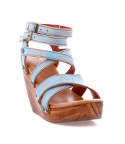 The Juliana II by Bed Stu is a blue wedge sandal with buckled straps, a cushioned wooden sole, and an open toe design.