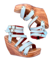 The Juliana II by Bed Stu is a pair of light blue wedge sandals featuring multiple straps, silver buckles, and cushioned wooden platform heels.