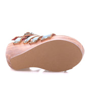 The Juliana II by Bed Stu is a brown platform sandal featuring metallic straps and a wooden heel, viewed from the side on a white background.