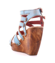 The Juliana II by Bed Stu is a blue strappy high wedge sandal showcasing a wooden heel platform with metal studs, viewed from the side on a white background. Its unique design includes artisanal hand-finishing.