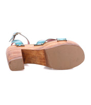 The Bed Stu Kalah is a wooden platform sandal featuring a chunky, sustainably sourced wooden heel, blue straps, and a rubber sole, shown from the bottom.