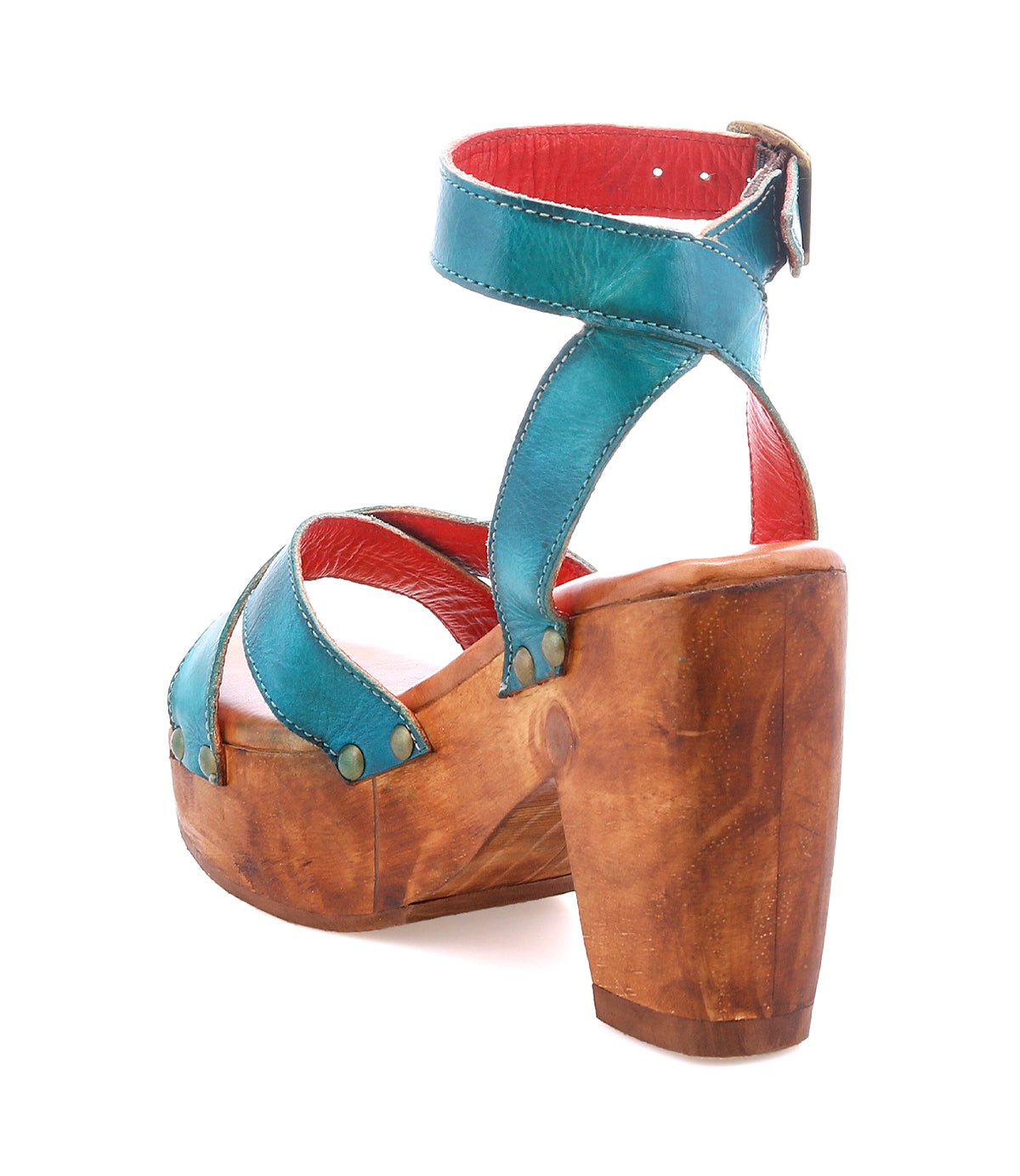 The Bed Stu Kalah is a teal leather sandal with an ankle strap, sustainably sourced wooden platform heel, red interior lining, and metallic rivets.