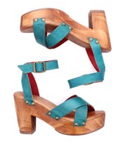 The Bed Stu Kalah sandals feature turquoise leather, crisscross toe design, ankle straps, and a sustainably sourced wooden platform heel, shown side by side against a white background.