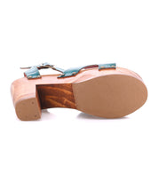 The Bed Stu Kalah sandal features a wooden sole, low block heel, and teal leather crisscross toe straps; shown from the bottom to highlight its sole and heel.