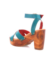 The Bed Stu Kalah is a teal leather sandal with a wooden block heel, crisscross toe design, ankle strap, and red interior, shown in profile against a white background.