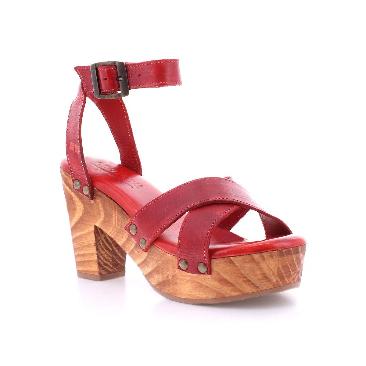 The Kalah sandal by Bed Stu is a red leather sandal featuring a chic combination of a wooden block heel, an ankle strap, and elegant rivet details. With its stylish platform heel, this sandal is crafted with eco-consciousness in mind and made entirely from sustainably sourced materials, seamlessly blending style with sustainability.