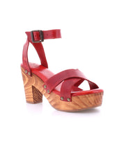 The Kalah sandal by Bed Stu is a red leather sandal featuring a chic combination of a wooden block heel, an ankle strap, and elegant rivet details. With its stylish platform heel, this sandal is crafted with eco-consciousness in mind and made entirely from sustainably sourced materials, seamlessly blending style with sustainability.