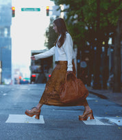A woman, channeling a 70s era vibe, crosses the city street in a white sweater and brown skirt. Her retro style is echoed by her chunky wooden platform shoes from Bed Stu's Karaoke collection as she carries a large brown bag.