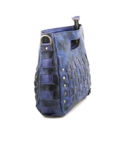 The Bed Stu Keiki is a blue leather crossbody bag featuring woven panels, metal rivets, and an integrated handle. It stands upright against a white background, showcasing its compact size and stylish texture.