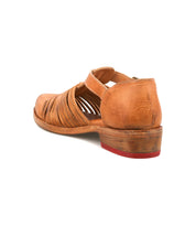 The Kenna by Bed Stu is a brown leather shoe with cut-out sides, overlapping woven details, a low wooden heel with a red sole accent, adjustable ankle strap, and closed heel.