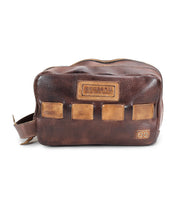 A brown leather dopp kit with a zipper, featuring a textured design crafted from vegetable tanned leather, a handle on the left side, and the brand "Bed Stu" embossed on the front. Perfect for travel essentials.