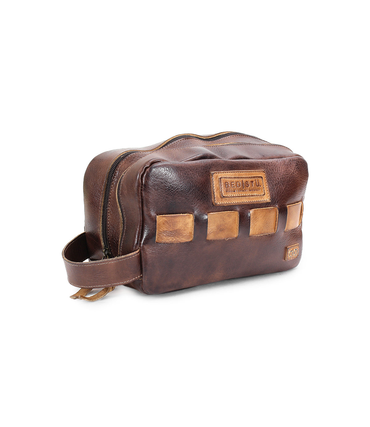 A handcrafted brown leather dopp kit with a zipper, a side handle, and decorative patches on the front. The brand "Bed Stu" is embossed on a leather patch, perfect for organizing your travel essentials. The product name is "Kip.