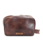A brown leather dopp kit with a zipper on top and a small handle on one side, crafted from premium vegetable tanned leather, perfect for your travel essentials. The Kip by Bed Stu is an ideal choice.