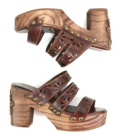 The Bed Stu Kreep sandals are brown wooden platform shoes with carved heels, three leather straps featuring floral cutouts and brass rivets, offering a unique individuality.