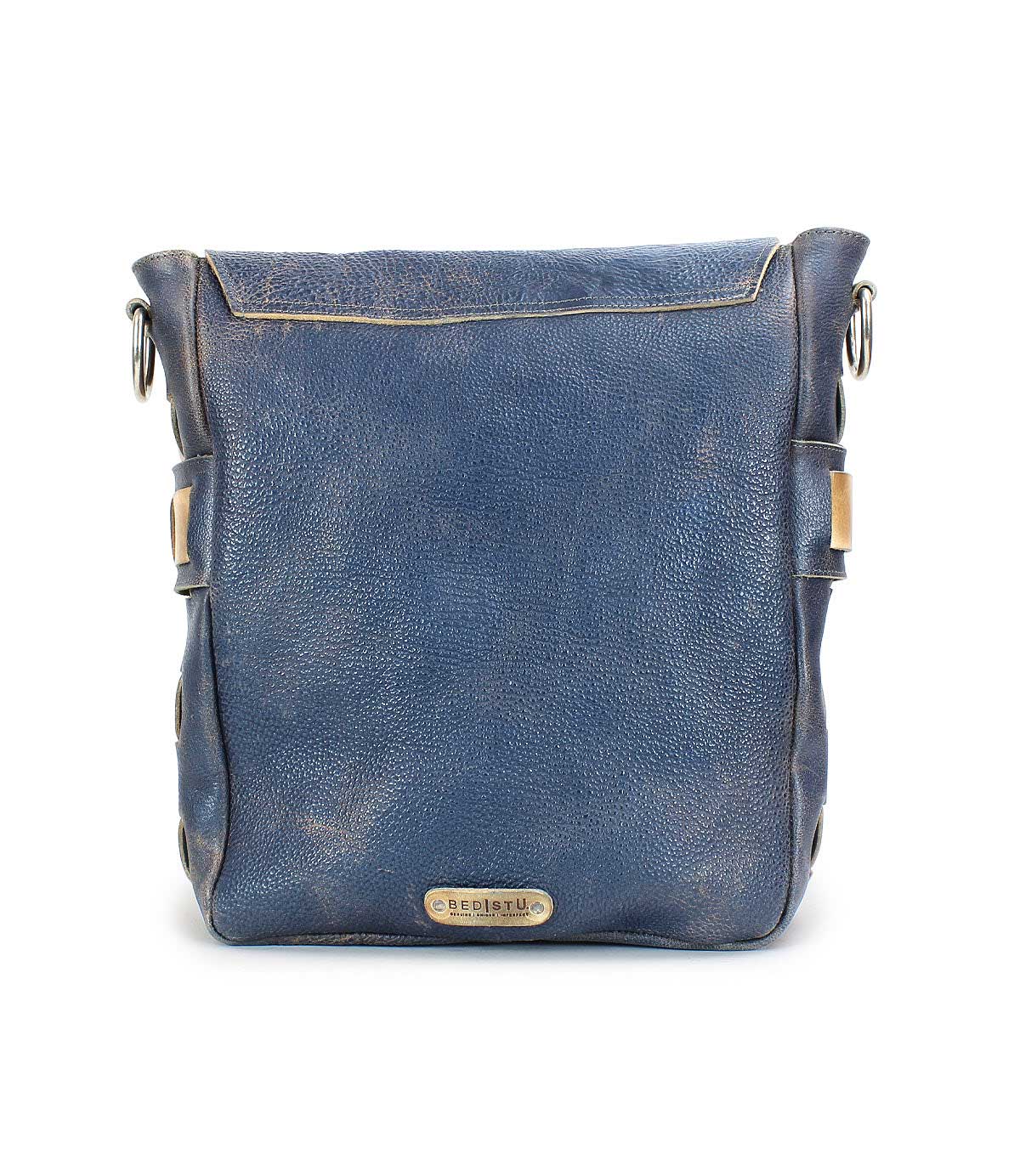 A square, dark blue handmade leather messenger bag with a metallic logo plate on the front, featuring side buckles, a flap closure, and an organic cotton-lined interior called Kure by Bed Stu.