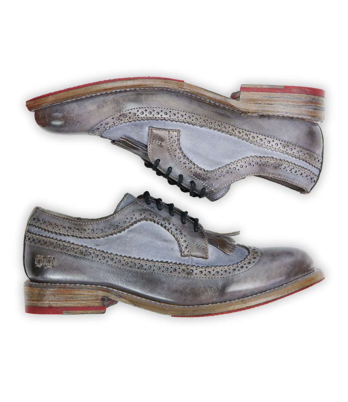 The Lita K shoes by Bed Stu, shown in side profile, are gray leather brogues with red-soled heels and a charming wingtip toe. The top shoe features black laces, adding a classic touch to the derby design.