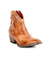 The Bed|Stü Laredoa is a tan leather ankle boot featuring a low heel, decorative stitching, floral cutouts, and a side zipper. Styled to showcase the front and outer side, this boot highlights its feminine cowboy boots-inspired silhouette and delicate floral cutout details.