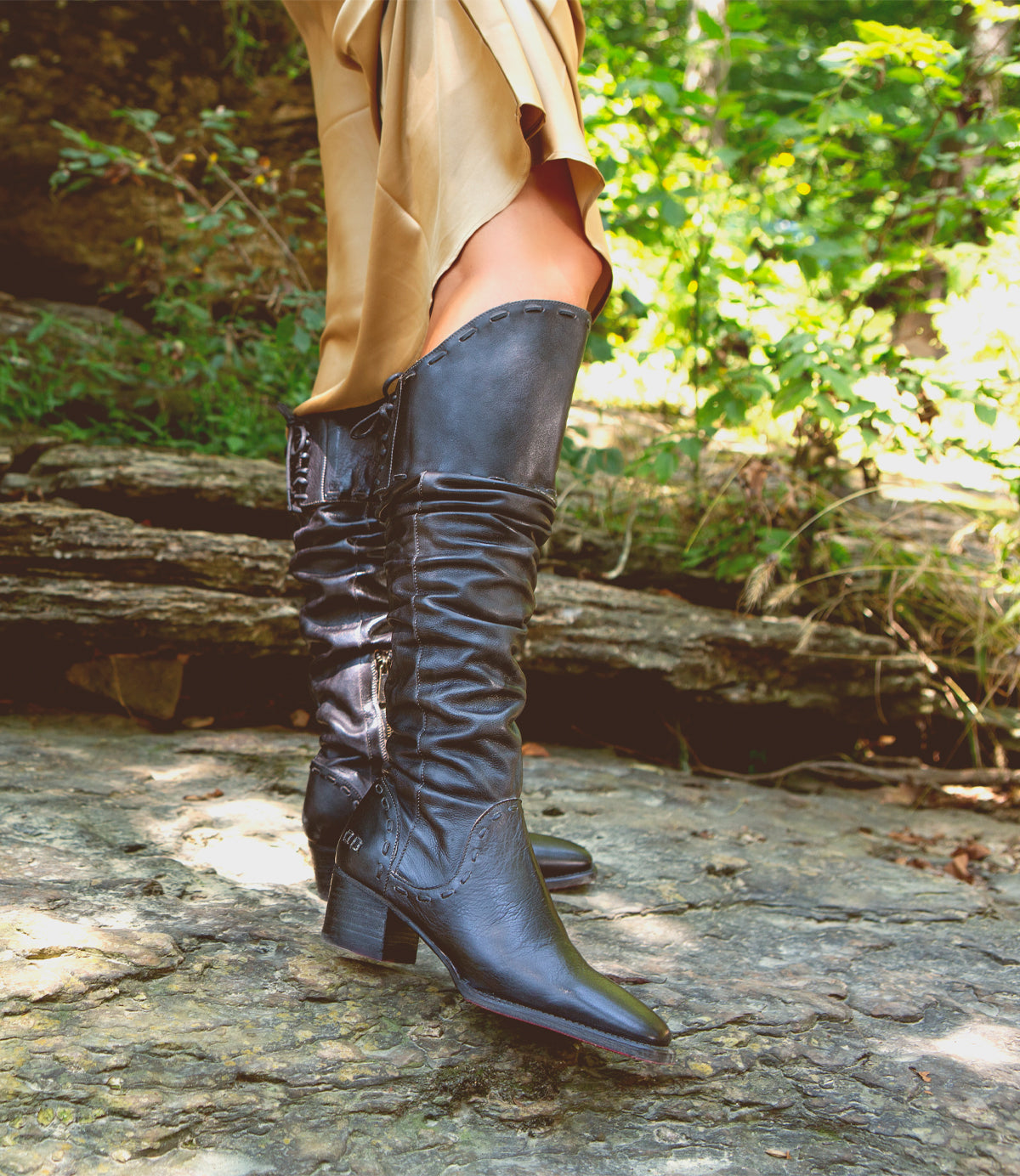 A woman in Bed Stu Leilani black boots standing on a rock in the woods.