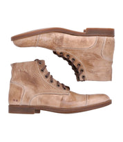 The Leonardo boots by Bed Stu are two tan leather lace-up boots with a distressed finish, positioned one above the other. These boots feature brown soles, visible stitching details, and comfortable insoles, complemented by a flexible rubber outsole for added comfort.