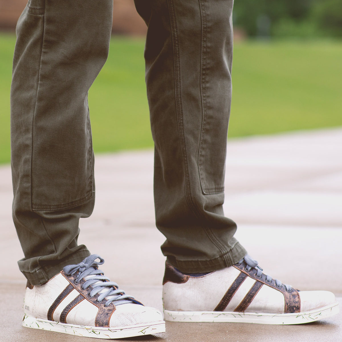 Person wearing brown pants and vintage Bed Stu Lighthouse low-top sneakers with brown stripes, standing on a wet surface outdoors.