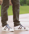 Person wearing brown pants and vintage Bed Stu Lighthouse low-top sneakers with brown stripes, standing on a wet surface outdoors.