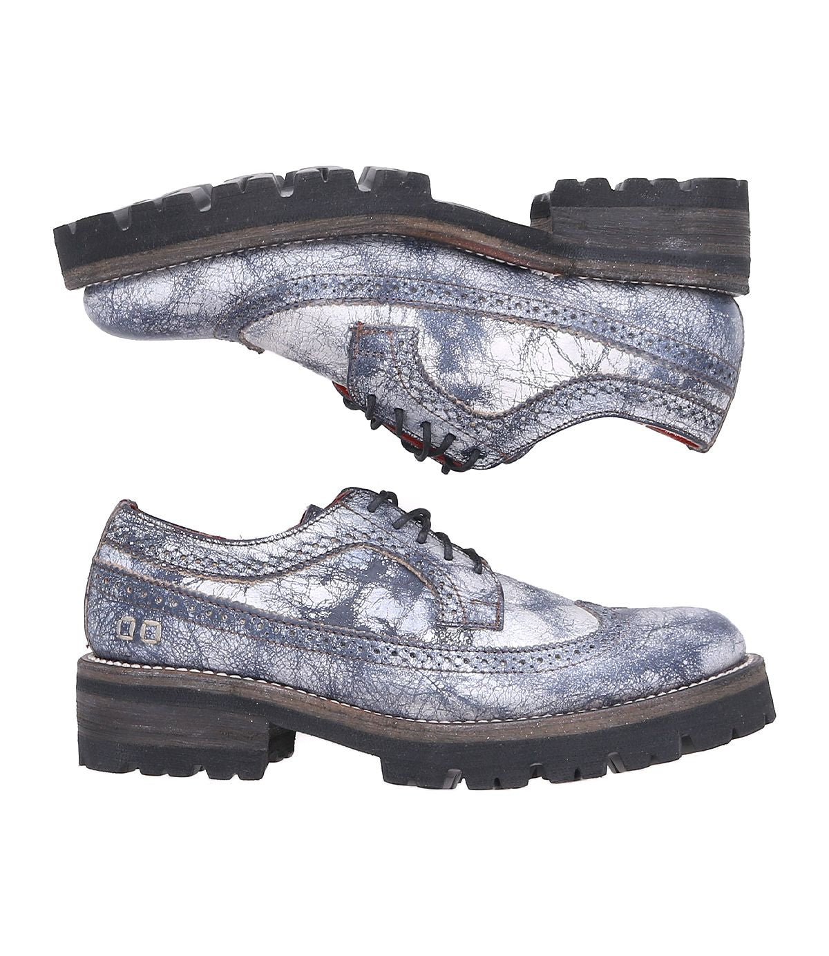 The Lita K III lace-up shoes by Bed Stu, featuring distressed metallic silver leather and chunky black soles that capture the essence of 90’s fashion, are stylishly positioned with one shoe on top of the other.