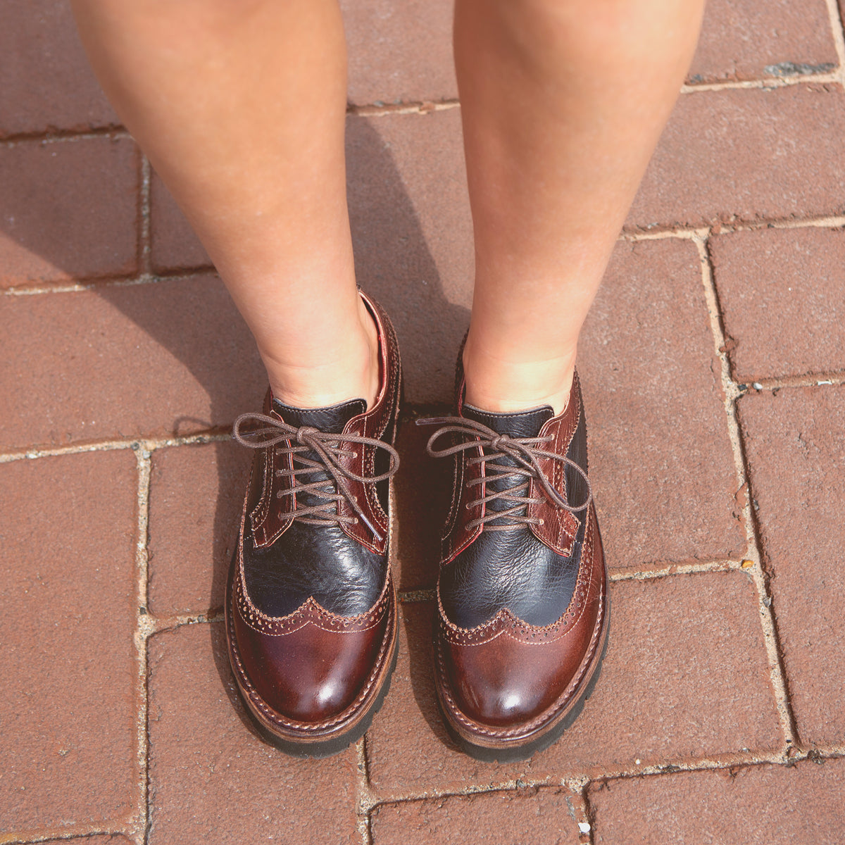 A pair of Bed Stu Lita K III brown leather wingtip shoes on brick pavement, viewed from above, epitomizing retro chic.
