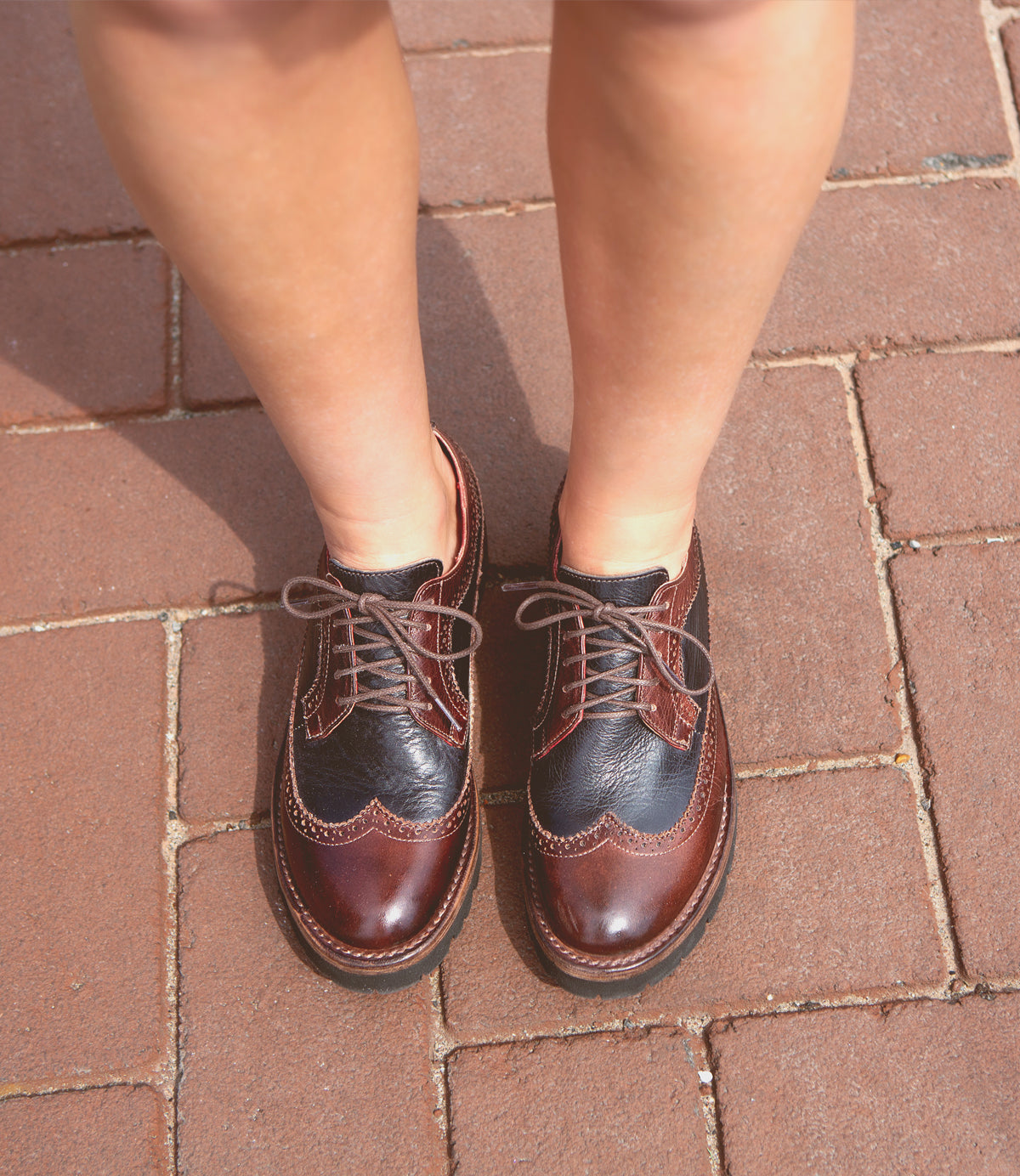 A pair of Bed Stu Lita K III brown leather wingtip shoes on brick pavement, viewed from above, epitomizing retro chic.