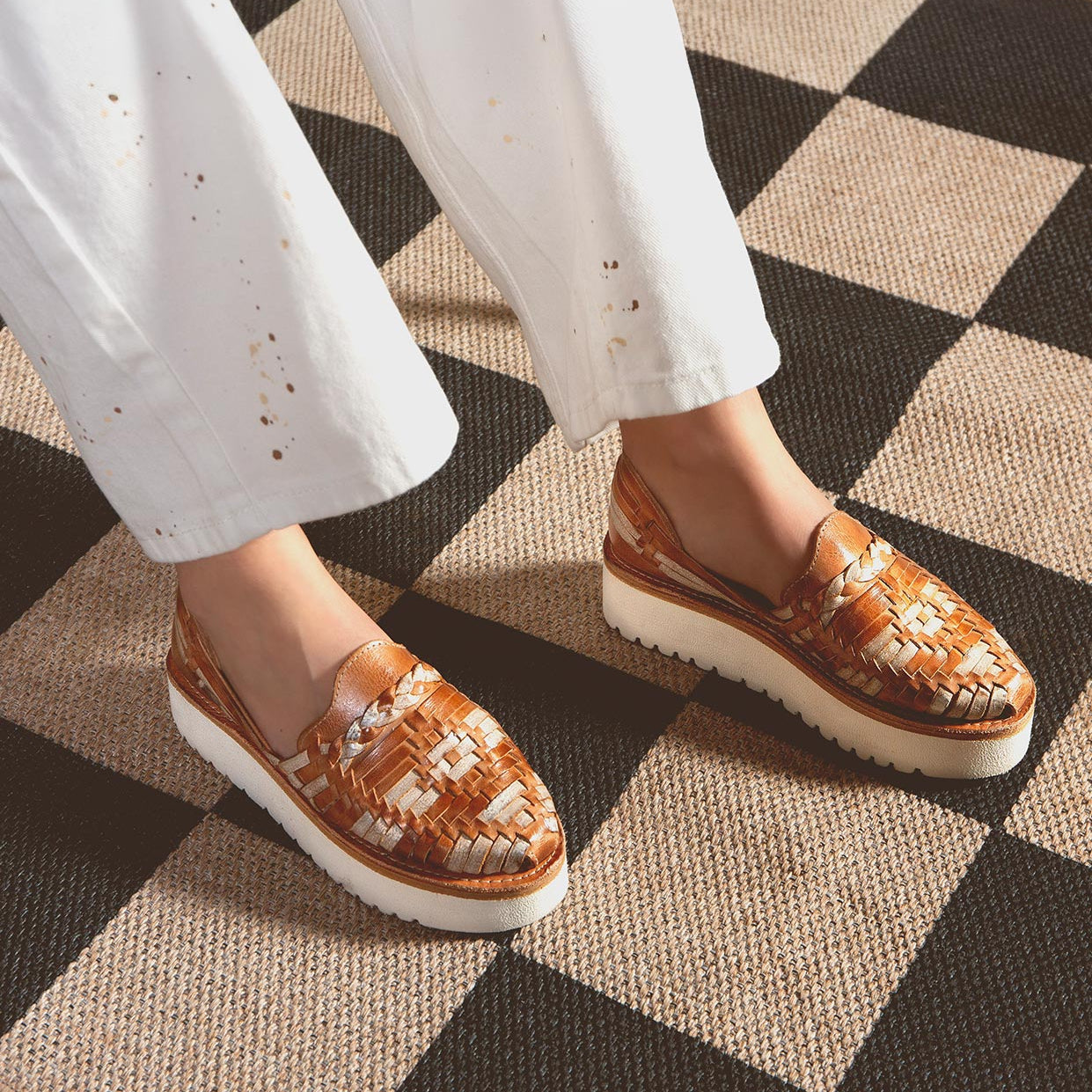 A person stands on a checkered floor in Bed Stu's Lizzie slip-on shoes and white pants, highlighting style and comfort with the durable XL EXTRALIGHT® outsole.