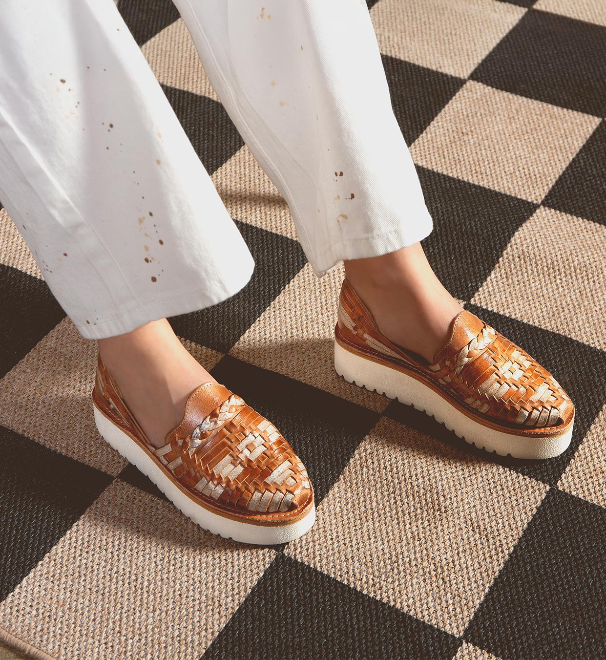 A person stands on a checkered floor in Bed Stu's Lizzie slip-on shoes and white pants, highlighting style and comfort with the durable XL EXTRALIGHT® outsole.