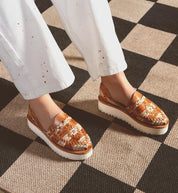 A person stands on a checkered floor in Bed Stu's Lizzie slip-on shoes and white pants, highlighting style and comfort with the durable XL EXTRALIGHT® outsole.