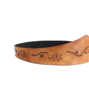 The Lucen belt by Bed|Stü features brown leather in a boho-chic style, adorned with floral engravings and a dark inner lining, displayed against a white background to create an expressive accessory for any outfit.