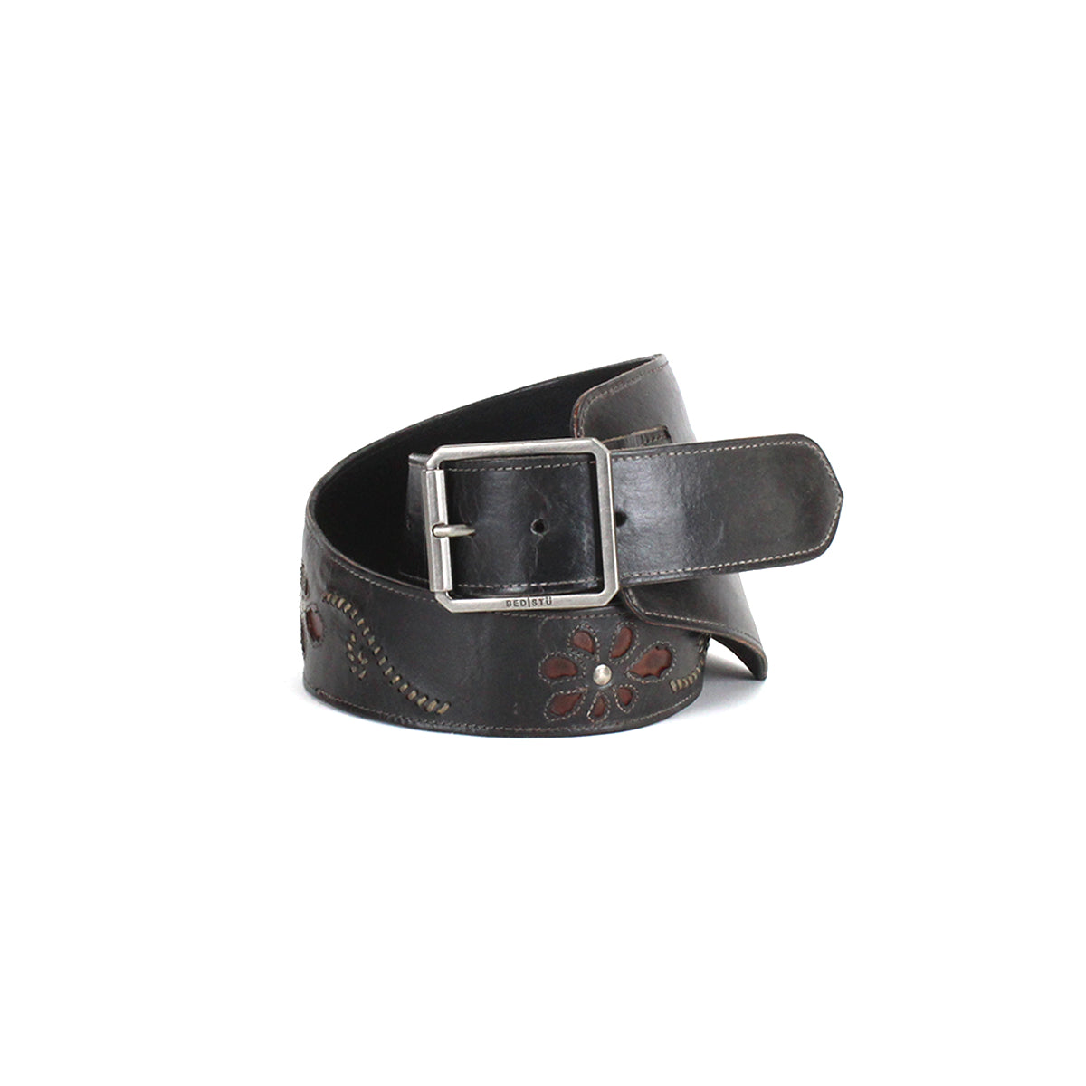The Bed|Stü Lucen is a wide, dark leather boho-chic belt featuring a silver rectangular buckle and floral cutout patterns; shown coiled on a white background, this expressive accessory adds stylish flair to any ensemble.