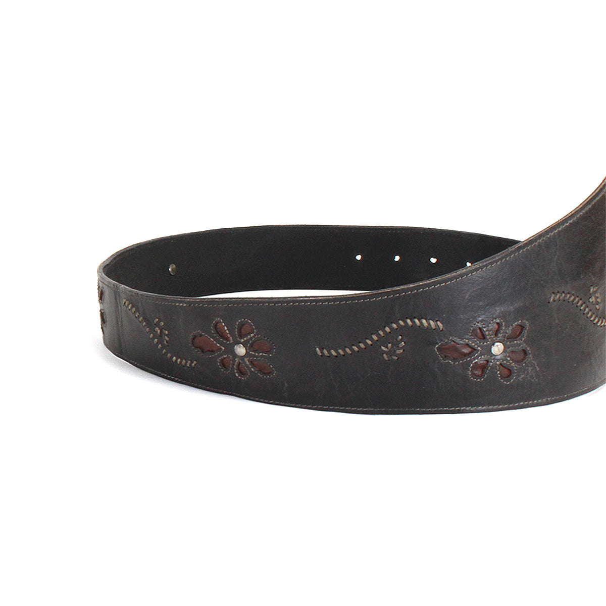 The Bed|Stü Lucen belt, featuring dark leather with boho-chic floral patterns and decorative stitching, is partially coiled on a white background and serves as a striking accessory that infuses any outfit with personality.