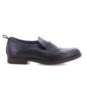Introducing the Bed|Stü Lumaro: a black distressed leather penny loafer featuring a low heel, decorative upper strap, and back pull tab, displayed in side profile against a white background.