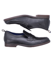 Two black Lumaro penny loafers by Bed|Stü, crafted from supple distressed leather with low brown heels, are displayed side by side—one upright and one sideways—to showcase different angles and the flexible loafer design.