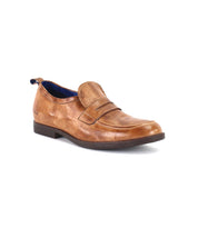 The Bed|Stü Lumaro is a single men’s loafer crafted from brown distressed leather, featuring a low heel, dark sole, and a decorative strap across the upper, photographed against a white background.