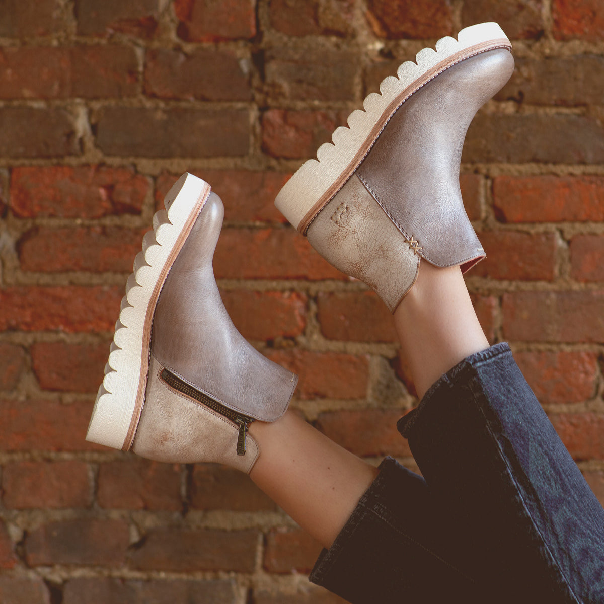 A versatile woman's legs in a pair of Bed Stu Lydyi ankle boots against a brick wall.