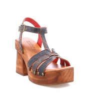 The Lyxon by Bed Stu is a brown leather sandal featuring a wooden block platform heel, open toe, ankle strap, and metal rivet details on the upper and sole.