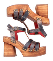The Bed Stu Lyxon sandals feature brown wooden block platform heels, black distressed leather t-strap design with metal studs and buckles, shown from side and top views.