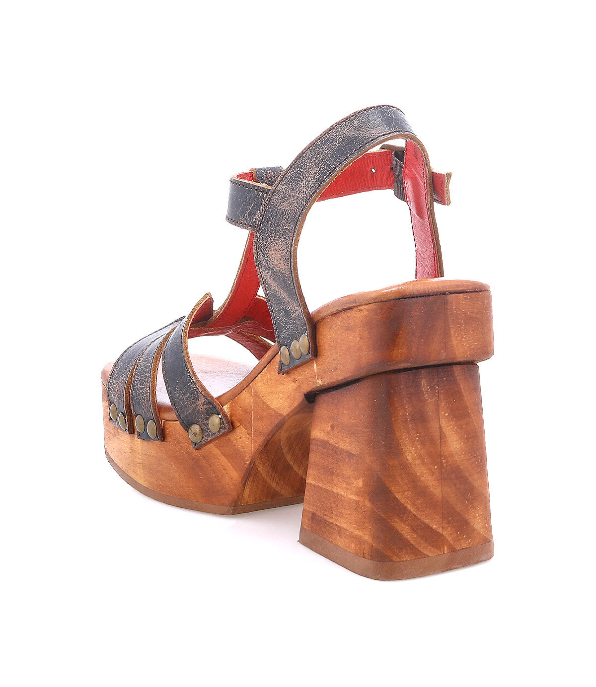 The Bed Stu Lyxon is a high-heeled sandal featuring a chunky wooden platform, dark leather T-strap design, open toe, and metal rivets, displayed from an angled rear view.