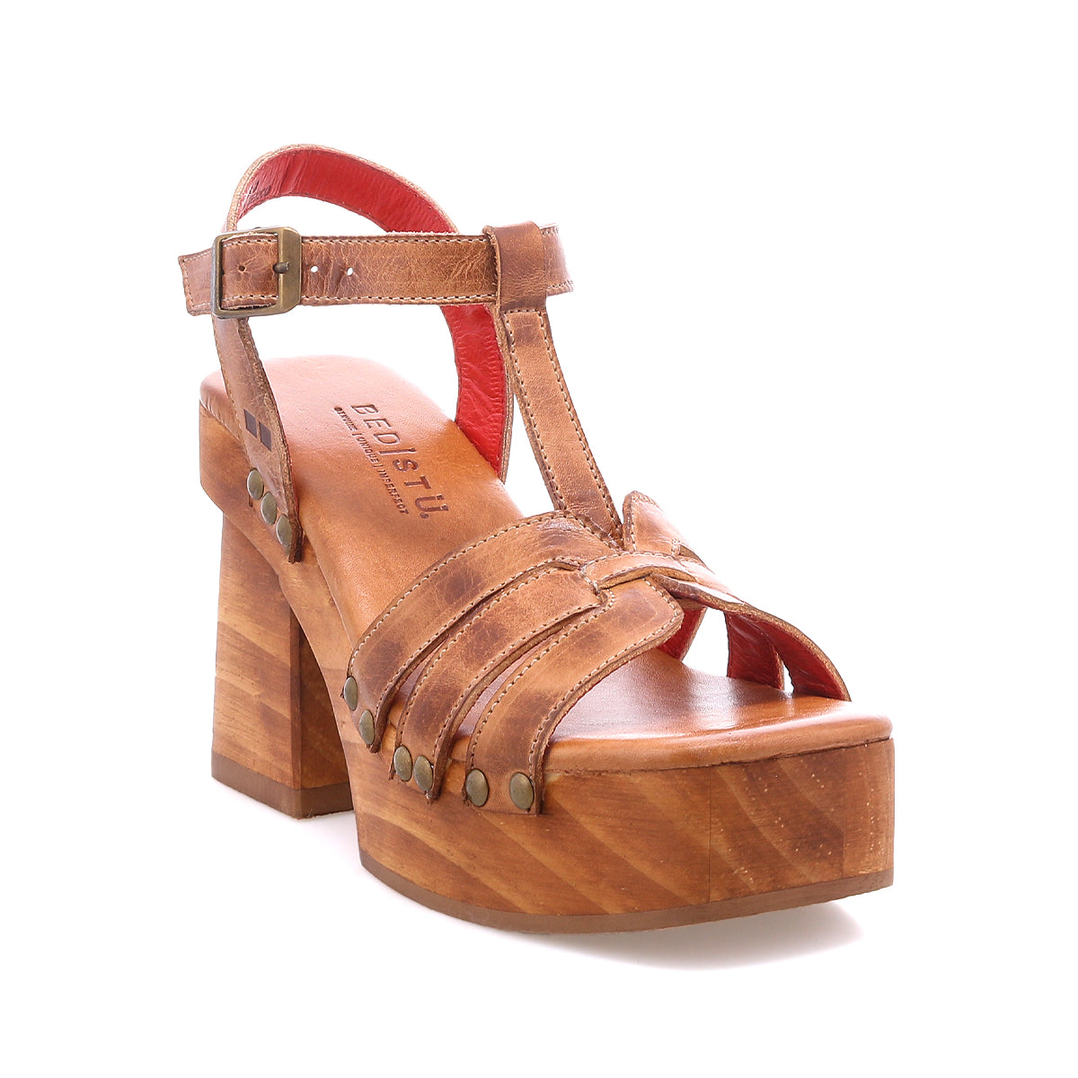 The Lyxon by Bed Stu is a brown leather platform sandal featuring a chunky wooden heel, open-toe T-strap, metal rivet accents, and an adjustable buckle ankle strap.