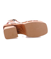 The image displays the Bed Stu Lyxon sandal’s bottom view, highlighting its thick, flat sole, low chunky heel with a wooden texture, tan rubber outsole, and open-toe design for added sturdiness.