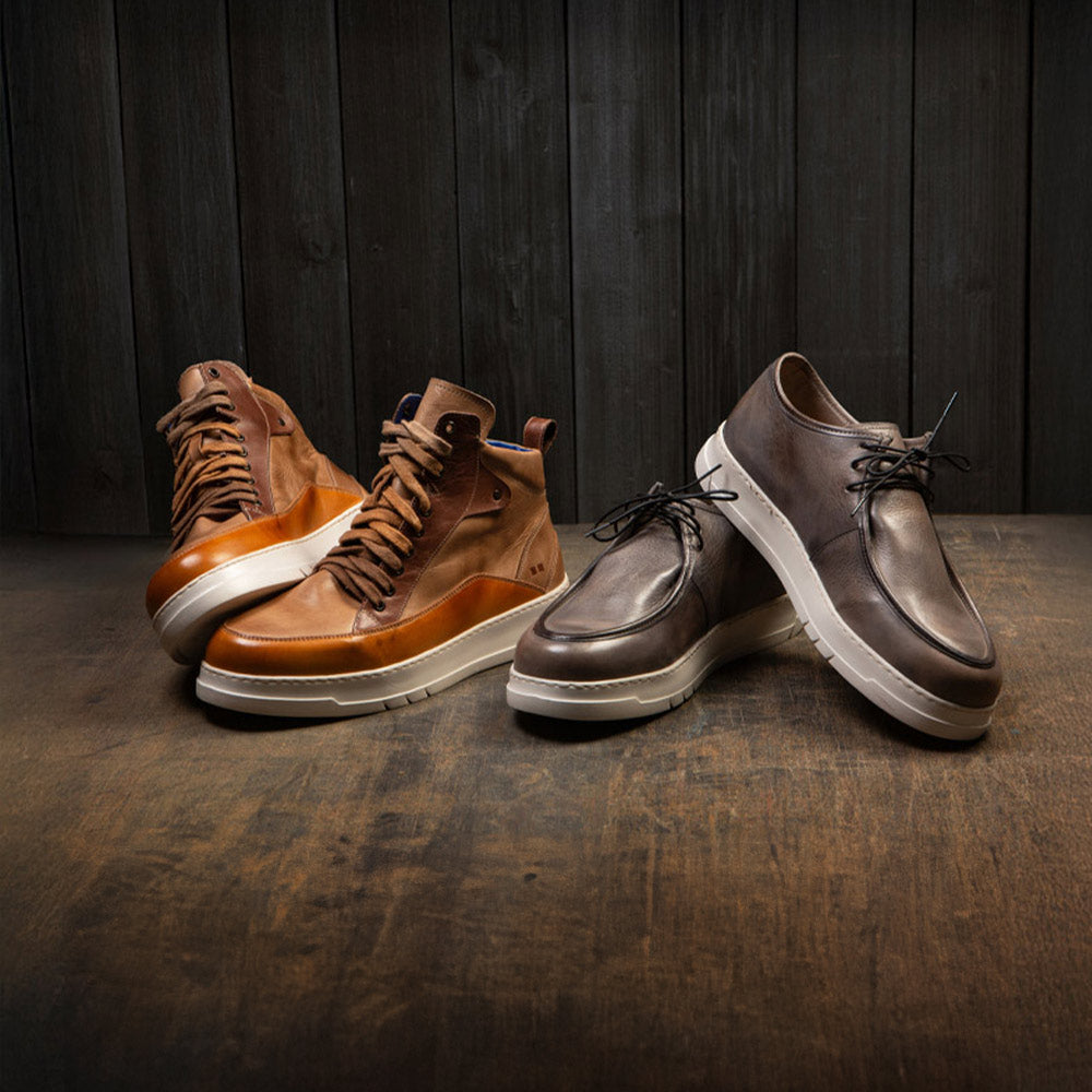 Two pairs of leather shoes on a wooden floor: tan high-top sneakers and dark brown lace-up shoes with light soles.