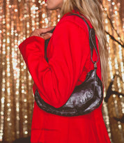 A person in a red jacket holds the Madre shoulder bag by Bed Stu against a backdrop of sparkling lights, adding a rock 'n' roll edge to the scene.