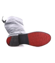 The Bed Stu Manchester boot, crafted in black leather, is shown on its side to reveal a red rubber sole with embossed patterns and a dark heel.