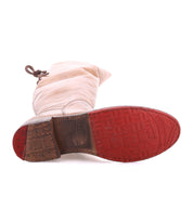 A Bed Stu Manchester boot in light beige, shown sole-up with a worn red tread, scuffed heel, and laces tied at the top.